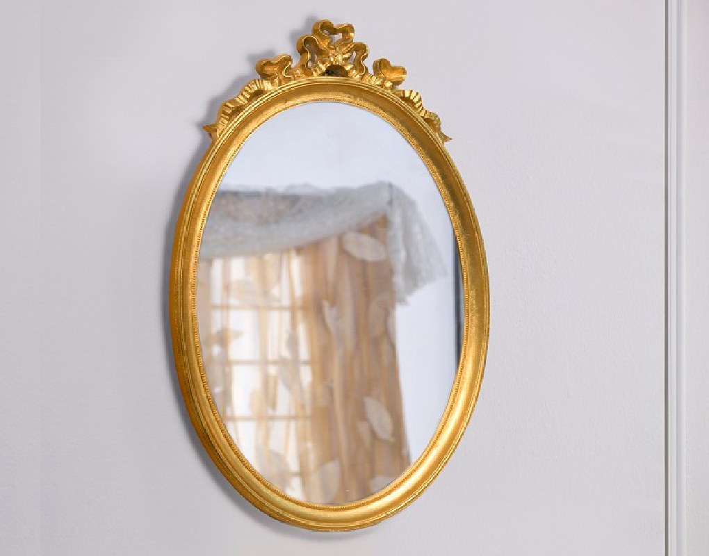 Barocker ovaler Spiegel mit ZierleisteGoldener verzierter Spiegel mit einem weißen Vorhang im Hintergrund.